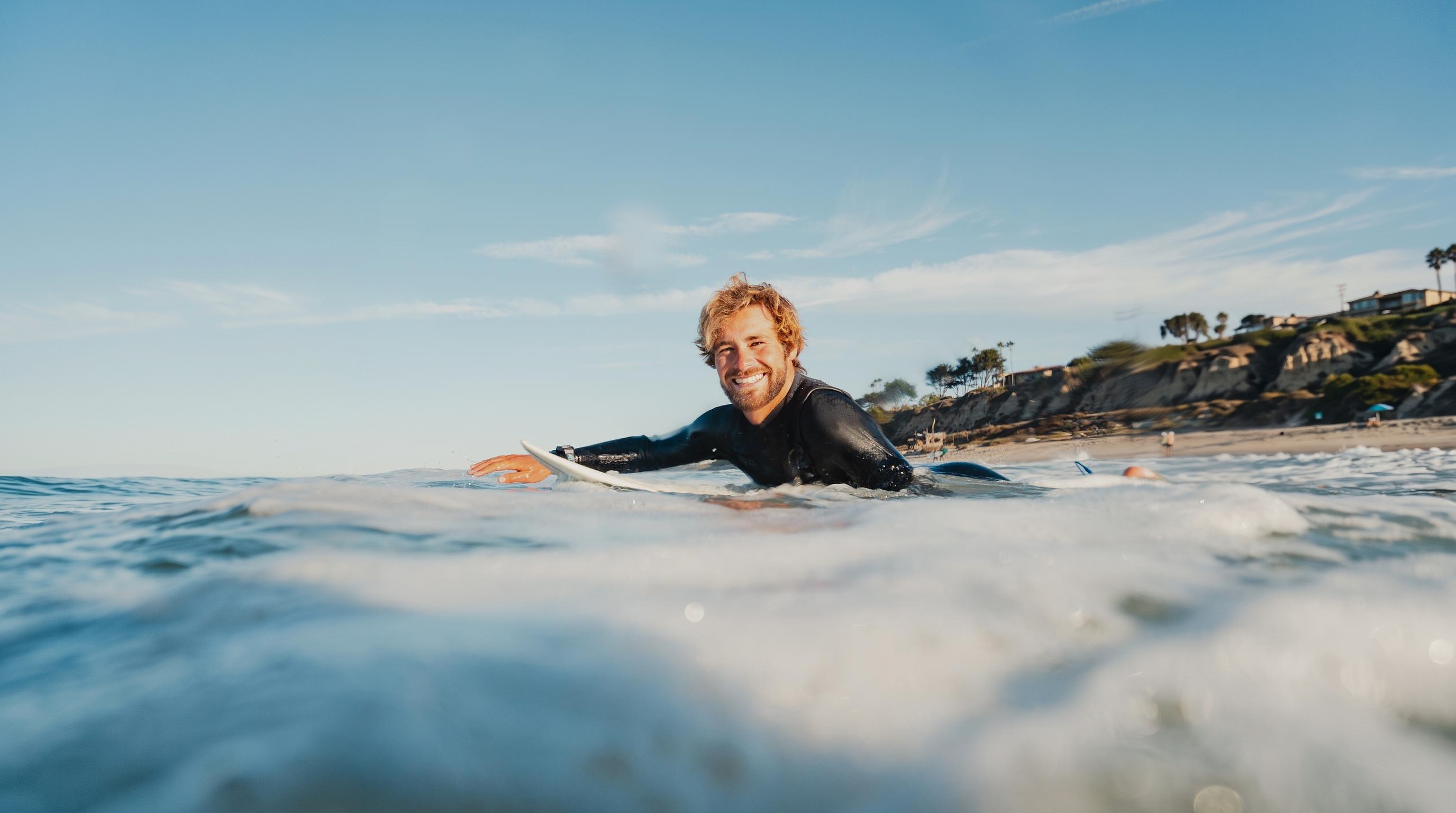 Lucas Taub smiling as he paddles out on his surfboard
