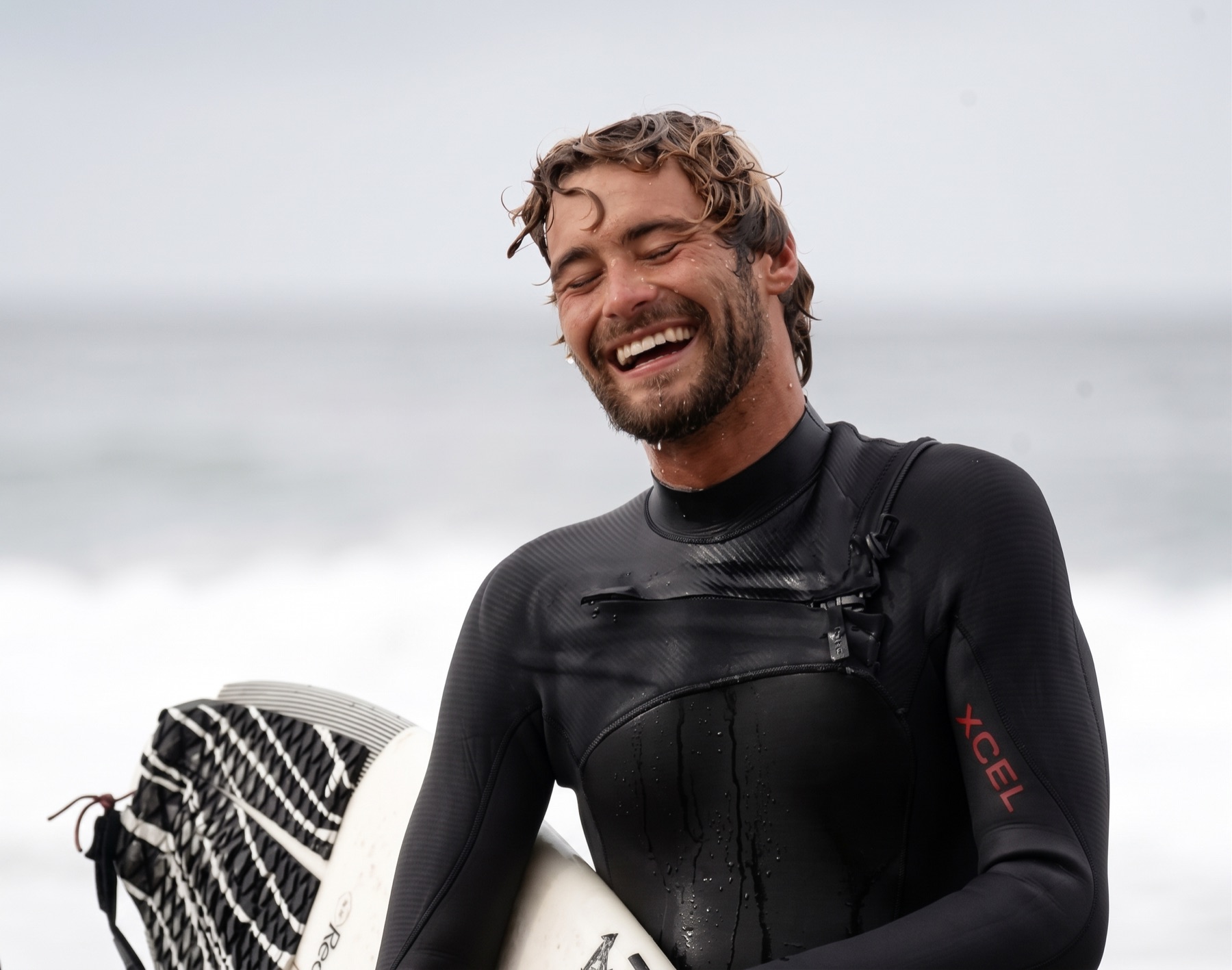 Lucas Taub, owner and head coach, laughing in his wetsuit with his surfboard