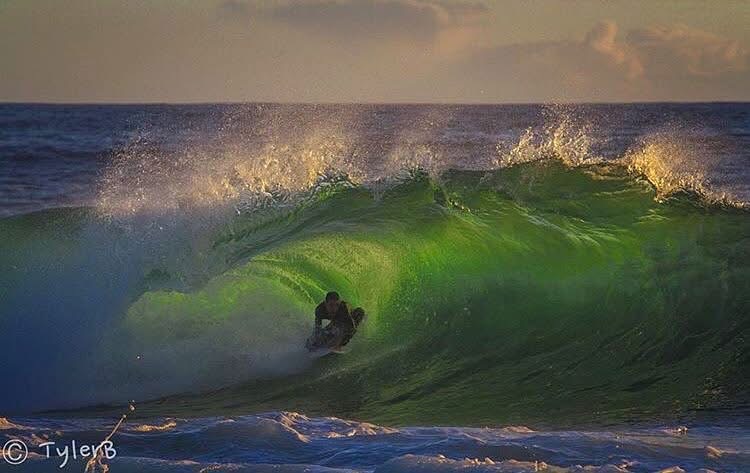 Surfer riding deep inside a glowing green barrel at sunset
