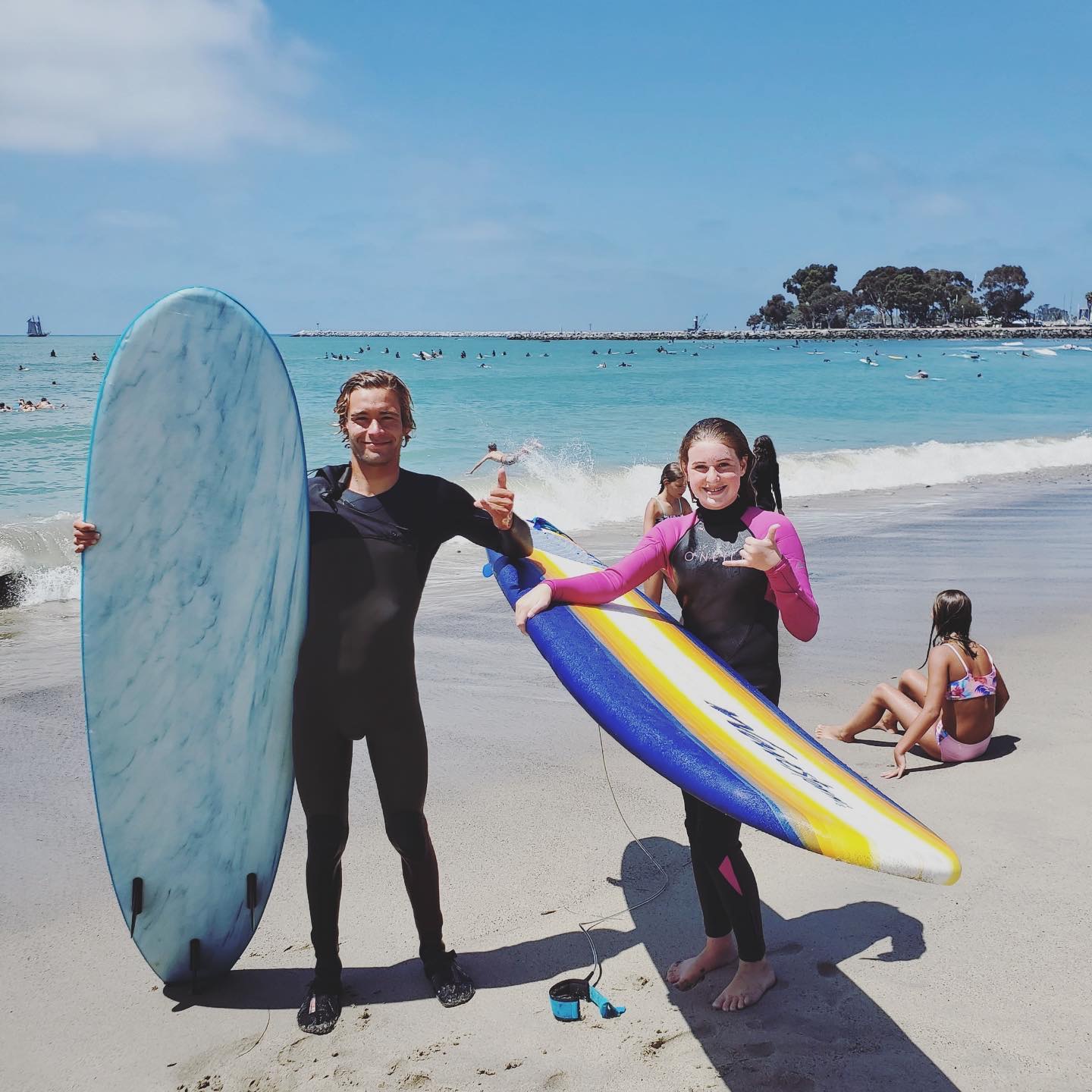 Coach and a smiling student holding soft-top surfboards on the beach